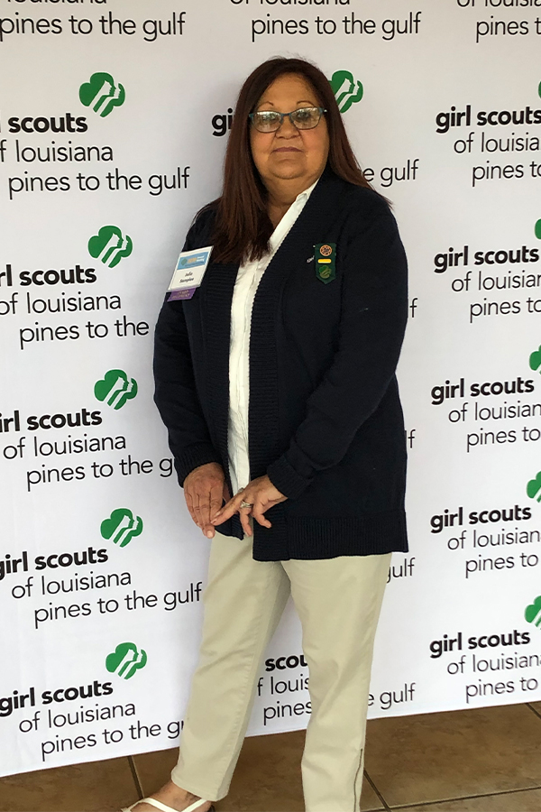 HedgeGuard Senior Benefits A woman stands in front of a "Girl Scouts of Louisiana Pines to the Gulf" step-and-repeat banner, wearing khaki pants, a white shirt, and a dark cardigan with a Girl Scouts pin, representing Simple Solutions Insurance with pride. HedgeGuard Senior Benefits A woman stands in front of a "Girl Scouts of Louisiana Pines to the Gulf" step-and-repeat banner, wearing khaki pants, a white shirt, and a dark cardigan with a Girl Scouts pin, representing Simple Solutions Insurance with pride.